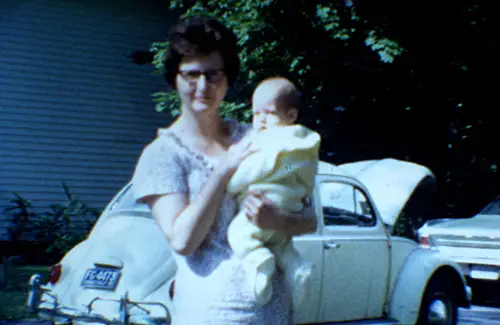 Grandma holding baby me in front of Tilly the VW Beetle