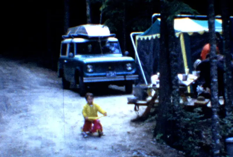 Young boy on a tricycle at a campsite with the International Scout behind him